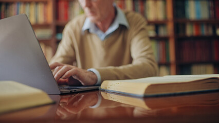 Male scientist looking for information in books and typing notes on laptop