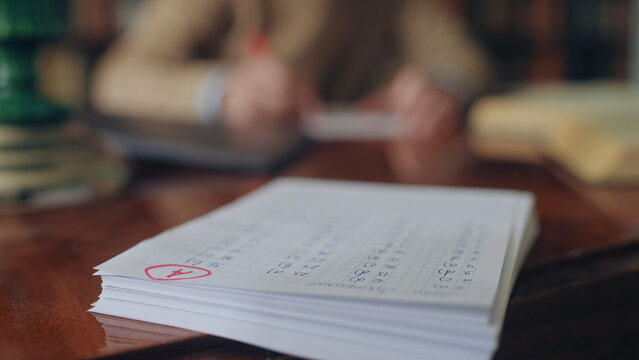 Stack of students test papers lying on teacher's desk, A grade on top sheet