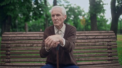 Elderly man with walking cane sitting on bench in park, resting after walk