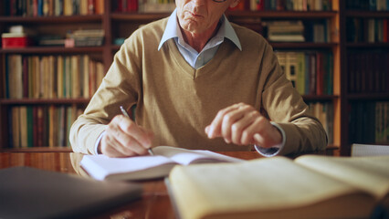 Senior male writer taking short notes in notepad, studying literature in a library