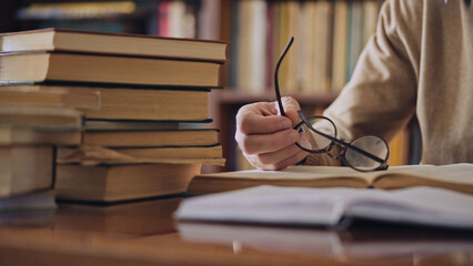 Male scientist taking off eyeglasses, resting from work with books in a library