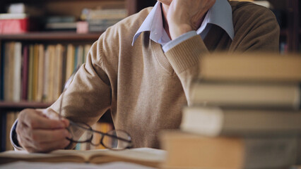 Male academic studying scientific literature in the library, pile of books on table