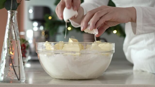 Cracking fresh egg into a bowl with flour and sugar to prepare dough for baking Christmas cookies