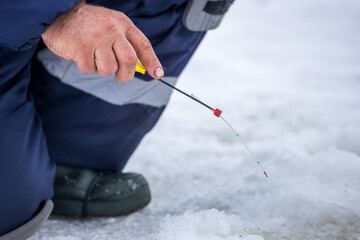 a fisherman on winter fishing sits with fishing rod by hole