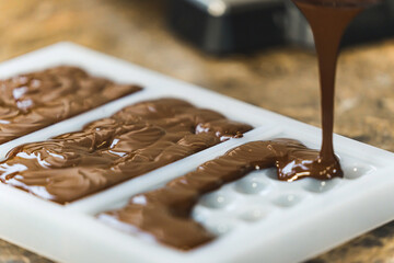 Craft brown chocolate liquid poured into a white bar mold to cool down. High quality photo