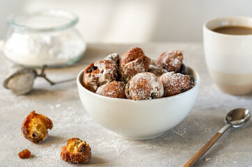 Italian traditional Carnival fritters toped with sugar powder in white bowl over concrete background with cacao mug and sugar in jar