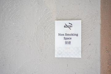 Square white paper no smoking sign on a wall in public place. No smoking sign is black line crossed cigarette smoke with English and Chinese letter means, No Smoking.