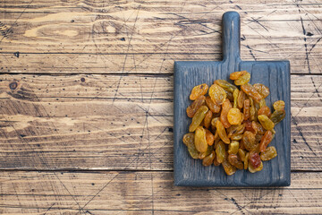 Dried raisins from white grapes on a wooden chopping board.