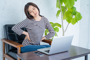 リビングでパソコン作業中に腰痛に悩む女性