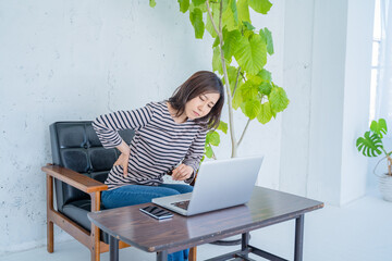 リビングでパソコン作業中に腰痛に悩む女性