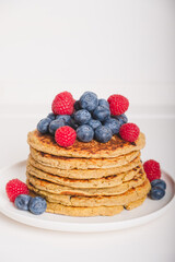 Delicious freshly cooked thick and fluffy gluten free pancakes stacked on white plate, served with fresh berries such as blueberries and raspberries. Healthy food. Place for text.