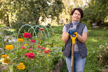 Mature woman standing relaxed near flowers with shovel in backyard smiling