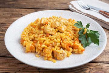 Delicious Asian pilaf, stewed rice with vegetables and chicken on a plate. Wooden rustic background.