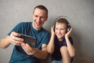 A cute boy with headphones is sitting next to his dad. Make a video call