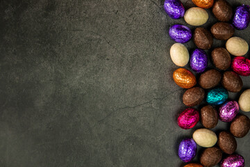 Delicious chocolate easter eggs ,sweets on dark black background,easter concept top view copy space wrapped colorful