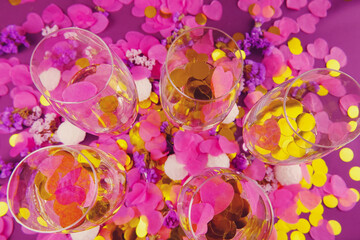 Wine glasses with sparkling wine on a lilac background and golden confetti.