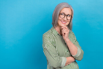 Naklejka na ściany i meble Photo of thoughtful minded smart retired business lady grey hair wear glasses look empty space problem solve isolated on blue color background