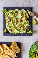 Butter board with broccoli, anchovies, nuts on black stone cutting board, bread slices, broccoli, concrete background