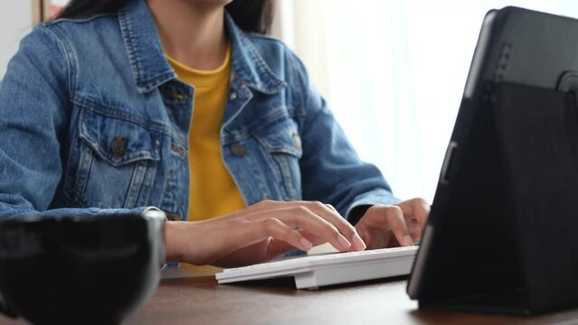 Young female employee in jean shirt working online on computer in office. Close up on hands of a manager typing texts on a keyboard.