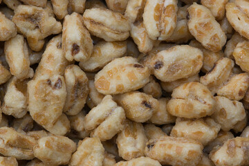 Dry honey puffed wheat cereal pieces scattered loosely directly above. Breakfast foods textured background, full frame image.	