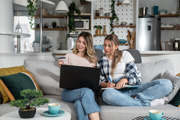 Two young women and best friends doing online shopping at home with a laptop and a credit card from web shop page sale while they smiling and they are happy. Females ordering food on internet