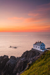 Lighthouse on the cliff edge at sunset