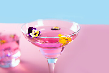Glass of pink violet purple cocktail decorated flowers viola pancies