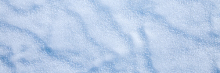 Beautiful winter background with snowy ground. Natural snow texture. Wind sculpted patterns on snow surface. Wide panoramic texture for background and design.