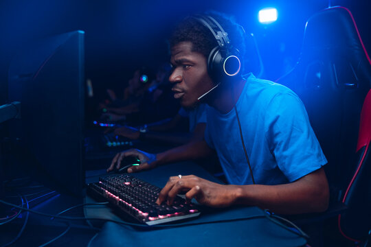 Gamer hacker African man with headphones, American player online video games in computer club esport multiplayer PvP, bokeh blur background color
