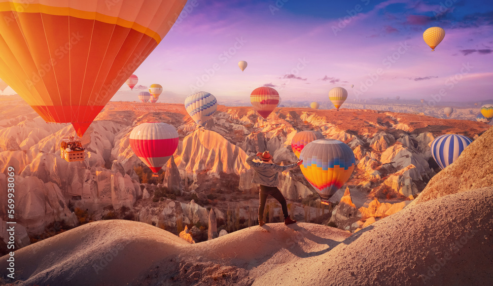 Wall mural Concept travel discoverer. Hiker man in hat on mountain background hot air balloons Cappadocia Turkey. Amazing adventure photo from aerial drone view