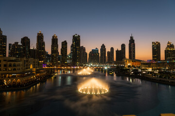 Fototapeta na wymiar Dubai singing fountains at night lake view between skyscrapers. City skyline in dusk modern architecture in UAE capital downtown.