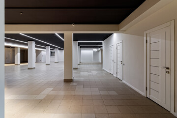 A large empty room with ceramic tiles on the floor, a black ceiling with lighting and columns propagating the ceiling