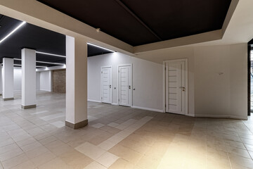 A large empty room with ceramic tiles on the floor, a black ceiling with lighting and columns propagating the ceiling