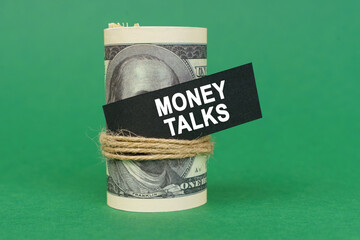 On a green surface, rolled dollars with a black sign that says - MONEY TALKS
