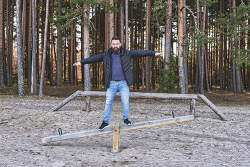 Adult bearded man hipster staying on swing at a play area in the forest. Concept of sanity, harmony and balance.