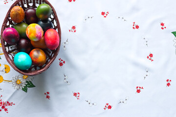 Top view of colored Easter eggs in a wooden basket on a white tablecloth background. Copy space.