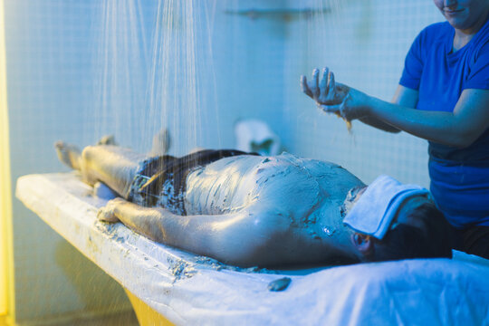 Professional therapist applying mud on client in spa center