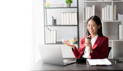 Portrait of young Asian businesswoman working and holding hot coffee cup in the office room.