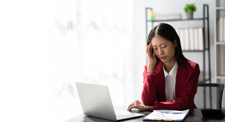 Tired Asian business woman with headache at office, feeling sick at work ater a busy day.