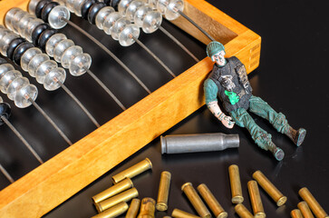 Toy plastic soldier without hand and cartridge cases lying next to wooden abacus (counting frame), black surface, military expenses theme, selective focus
