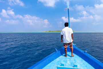 Mann auf einem Boot fährt zu einer kleinen Palmeninsel der Malediven