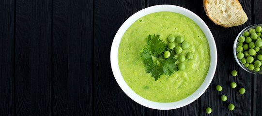 Pea soup in the white bowl on the black wooden background. Copy space. Top view.
