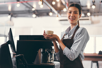 Beautiful Asia barista holding coffee cup with coffee machine in coffee shop	