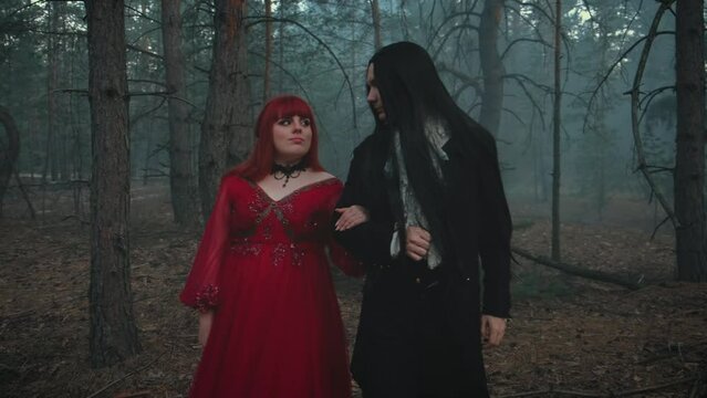 old film style. Romantic gothic medieval fantasy couple walking in deep dark forest tree. Vampire man king in black tailcoat long hair, guy holding hand of woman Queen. Look at each other with love 4k