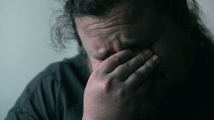 Desperate man crying in despair covering face in shame and regret. Person suffering from emotional...
