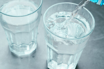 Pouring water from bottle into glass on grey background. Refreshing drink. Healthy lifestyle and stay hydrated