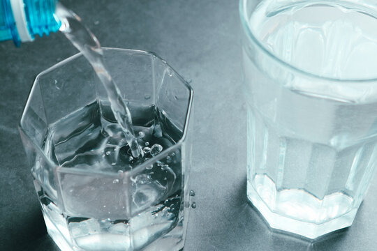 Pouring water from bottle into glass on grey background. Refreshing drink. Healthy lifestyle and stay hydrated