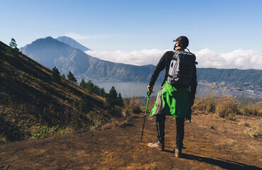 Anonymous male traveler with trekking pole standing on hill in highlands