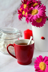red mug with tea on the background of a bouquet of red flowers