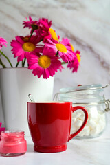 red mug with tea on the background of a bouquet of red flowers